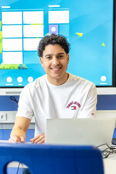 Jongeman achter laptop met groot beeldscherm achter hem