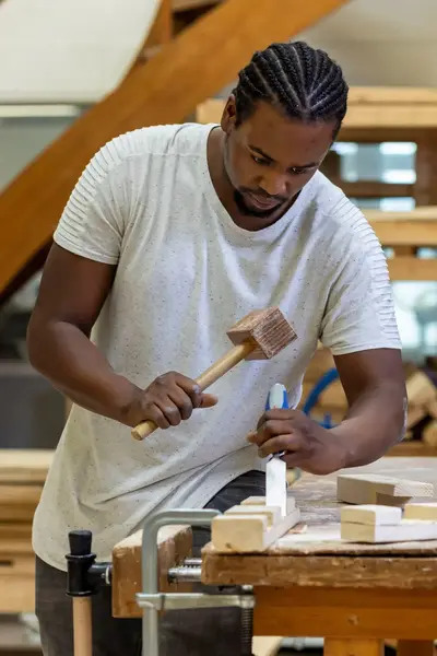 Student in praktijklokaal/timmerwerkplaats die aan het werk is met een hamer en een beitel.