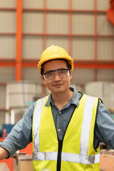 Man met gele helm en geel hesje tussen oranje machines