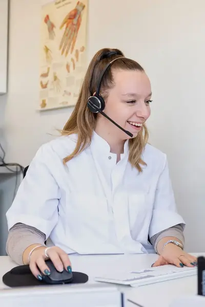 Student werkt op een computer met een headset op aan de balie van een medische praktijk.