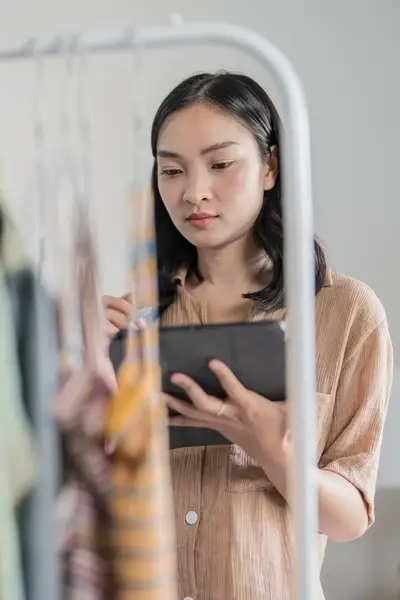 Studente met tablet inventariseert kledingvoorraad