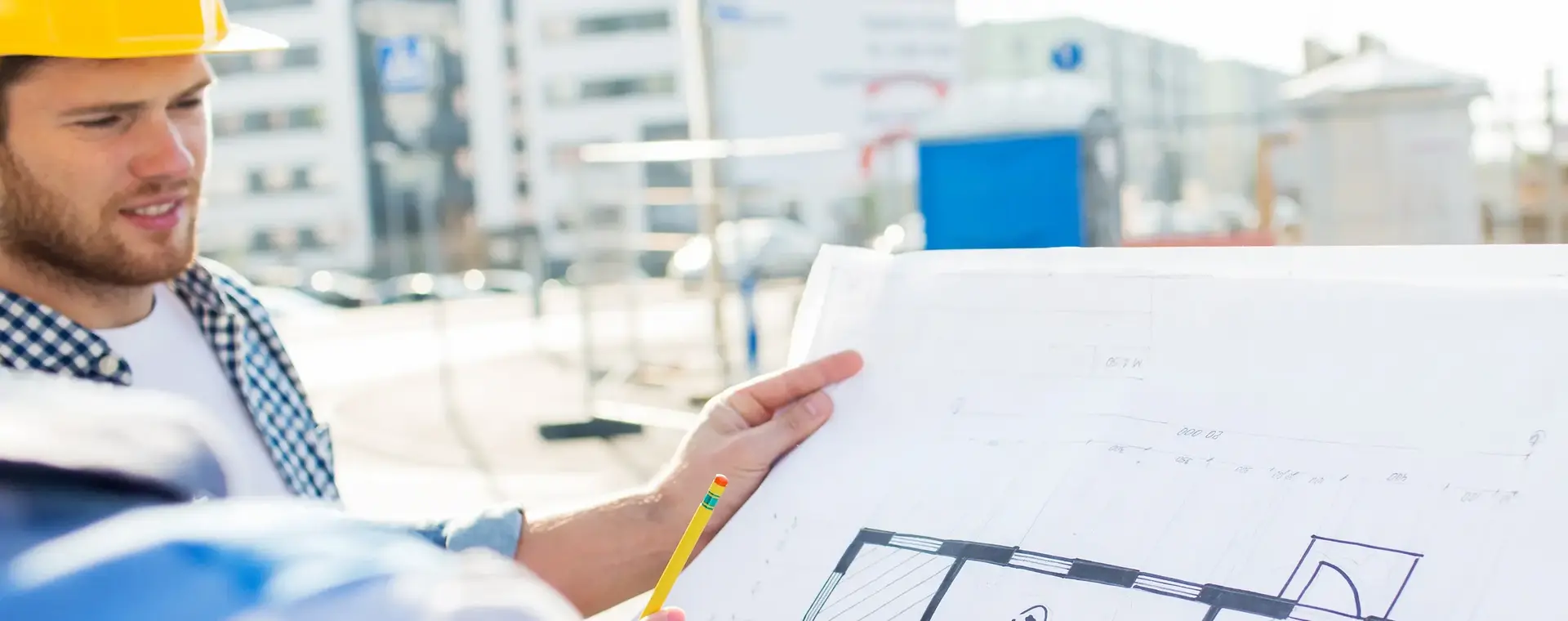 Jongeman met helm en bouwtekening op bouwplaats