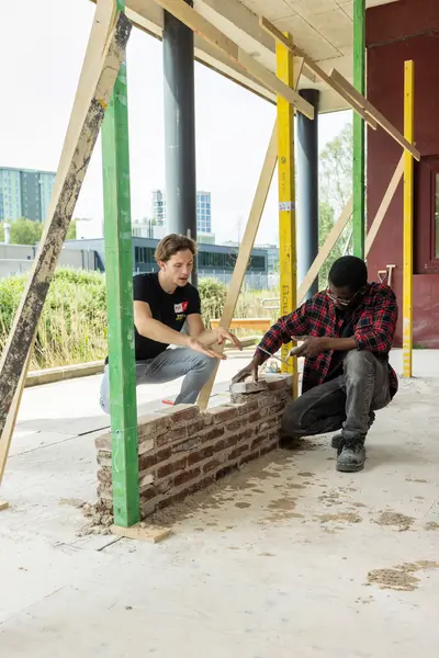 Student metselaar krijgt uitleg van docent op een bouwlocatie.
