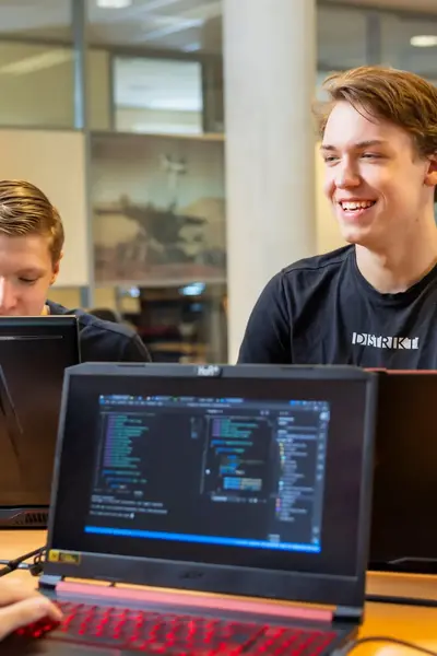 Studenten werken samen aan programmeeropdrachten met laptops in een klaslokaal