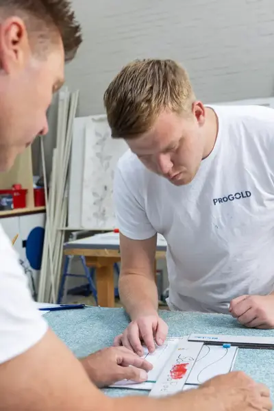 Twee schilders zijn bezig om iets op te meten aan een werktafel.