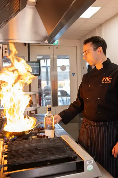 Student flambéert gerecht in een keuken met hoge vlammen.