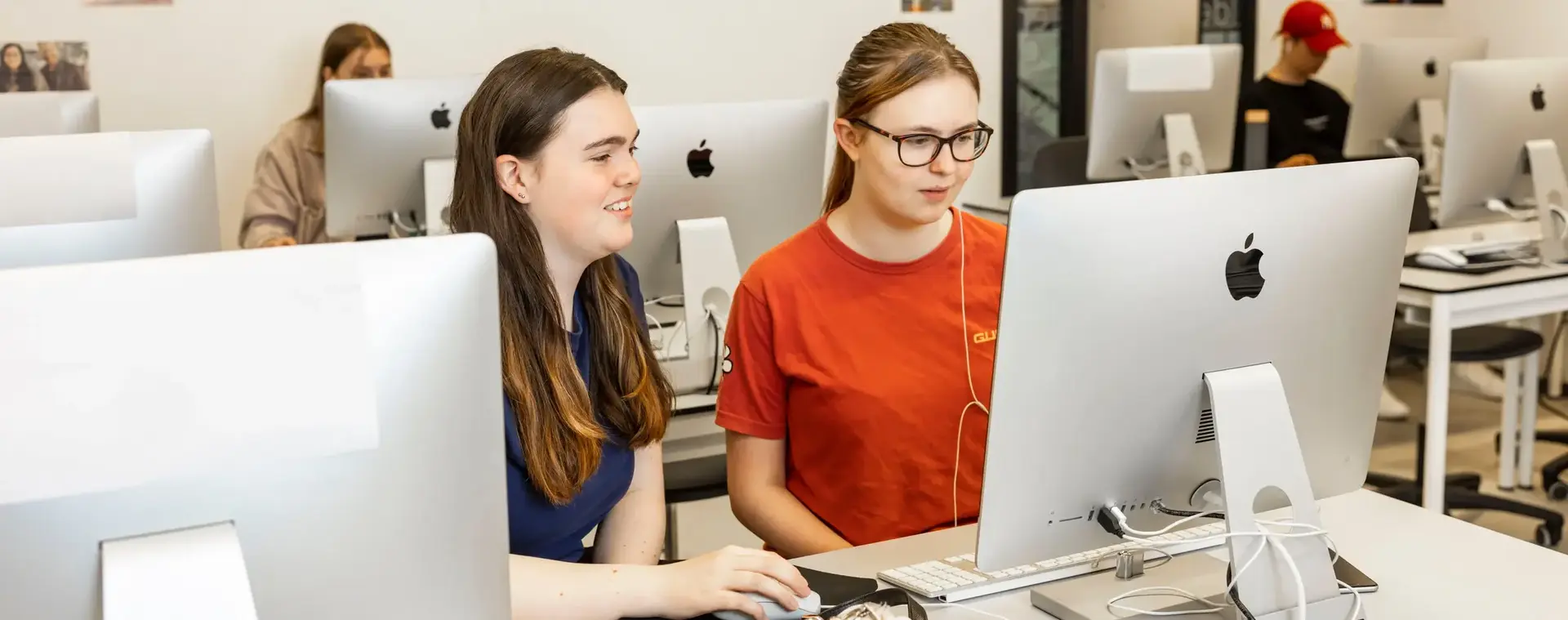 Twee studenten zitten achter een Imac-computer te werken.