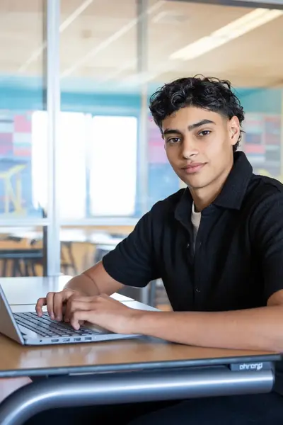 Jongeman achter laptop die in camera kijkt