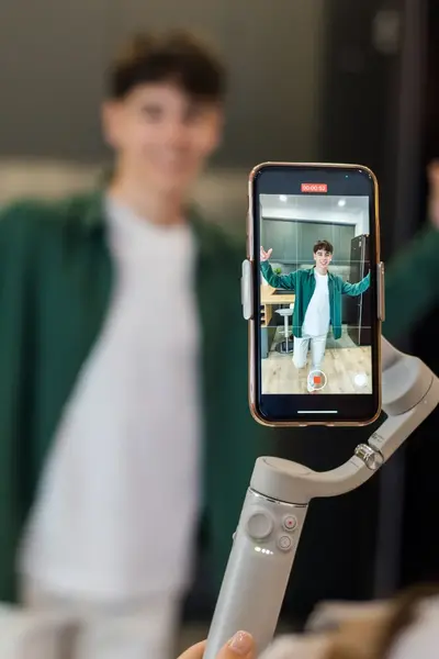 Studente houdt mobiel met selfie-stick vast en fotografeert een jongen.
