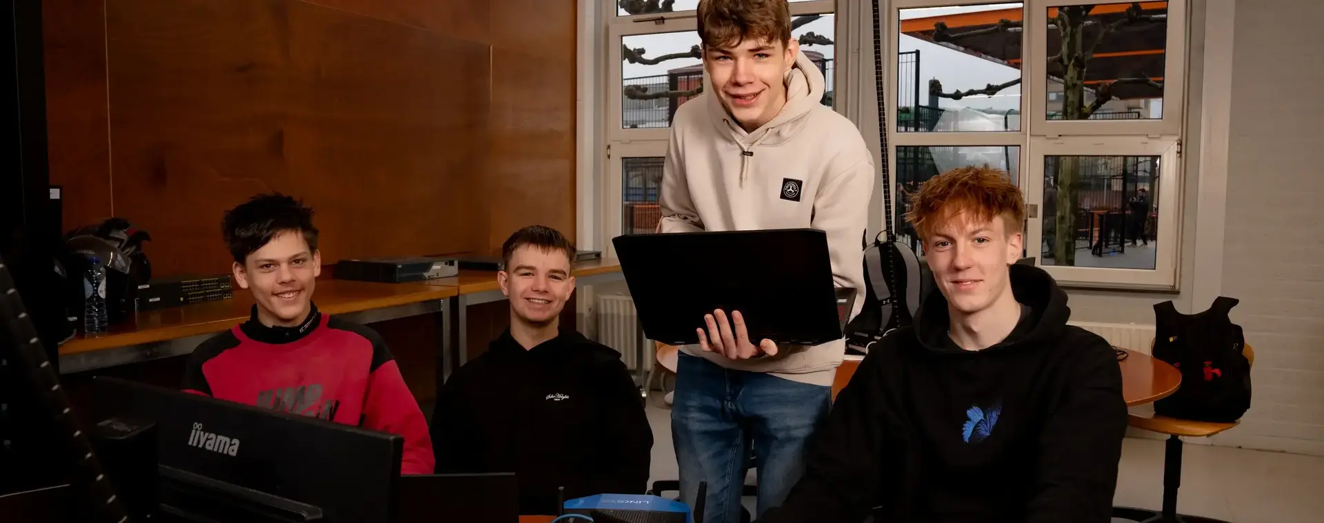 Vier studenten werken samen aan een game op hun laptops in een klaslokaal.