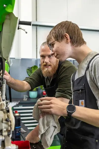 Student werkt samen met docent aan het onderhoud van een motorfiets in een werkplaats.