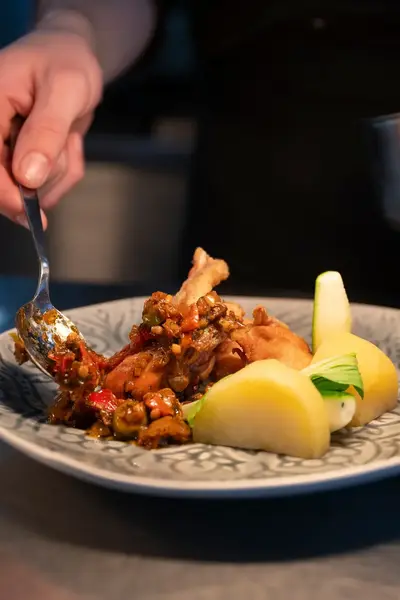 Chef die een gerecht met gestoofde kip, groenten en aardappels opmaakt.