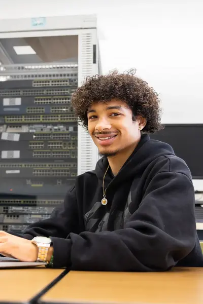 Student werkt op een laptop in een ICT-lokaal met netwerkapparatuur op de achtergrond.