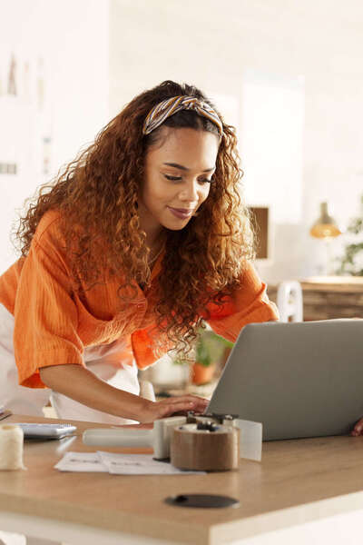 Jonge ondernemer werkt op laptop tussen kleding en dozen.