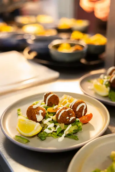 Een bord met falafel, sla, tomaatjes, citroen en witte saus staat klaar om geserveerd te worden.