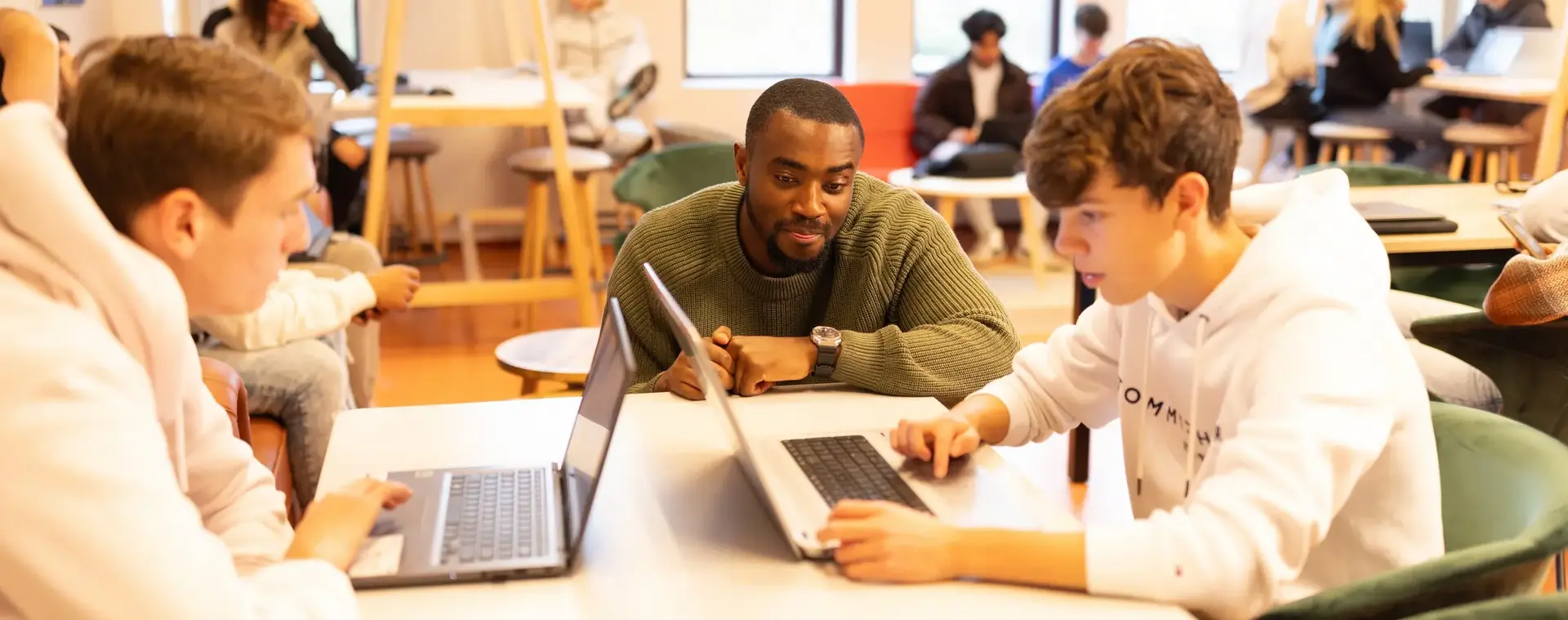 Studenten werken samen met docent op laptops in een klaslokaal.