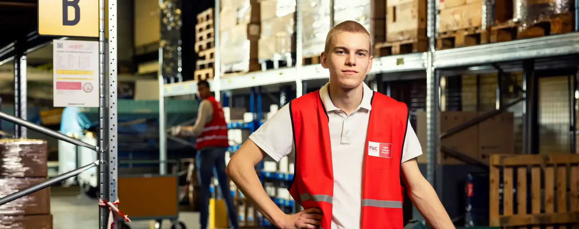 Jongen in oranje hesje met steekwagen in groot magazijn