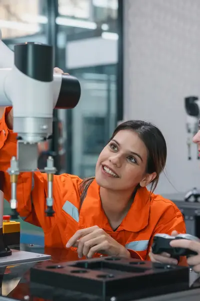 Twee vrouwen in oranje overalls bestuderen een robotarm