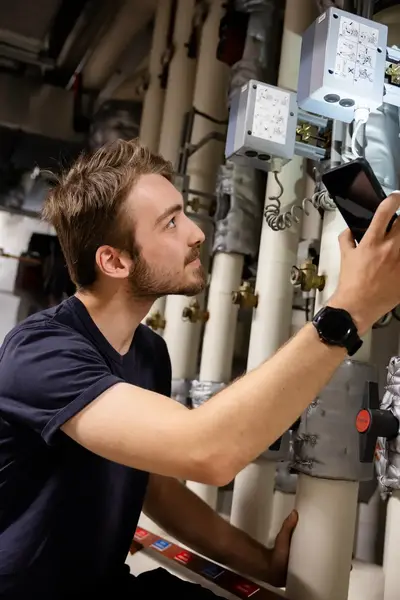 Student inspecteert buizen met behulp van de zaklamp op zijn telefoon.