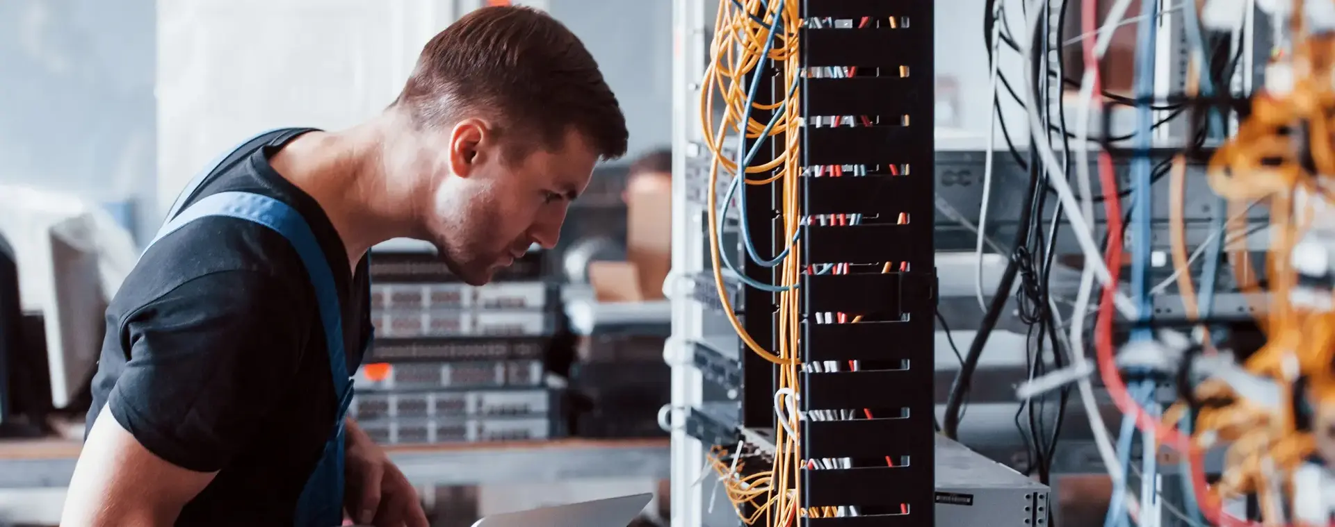 Een IT-technicus controleert netwerkkabels in een serverruimte terwijl hij gegevens invoert op een laptop, om verbindingen en systeemfunctionaliteit te testen.