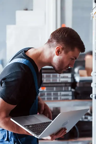 Een IT-technicus controleert netwerkkabels in een serverruimte terwijl hij gegevens invoert op een laptop, om verbindingen en systeemfunctionaliteit te testen.