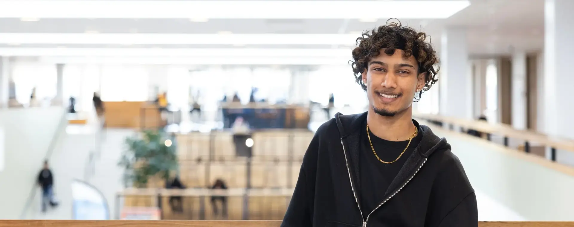 Student met zwarte hoodie glimlacht naar de camera.