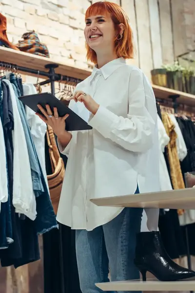 Kledingverkoopster met tablet in hand in winkel