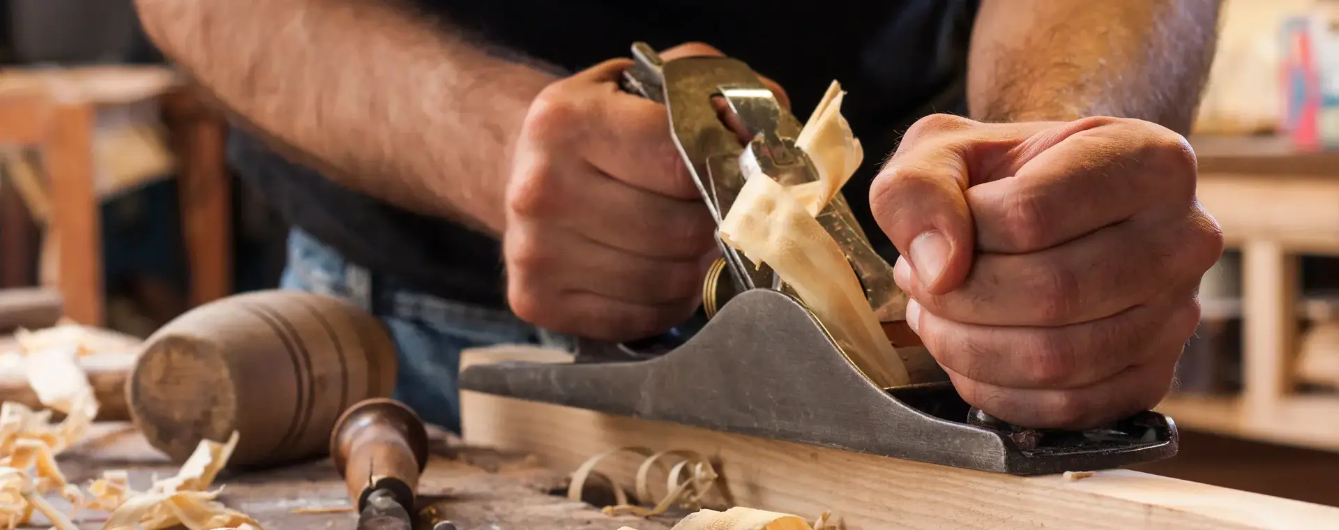 Twee handen die een plank schaven omringd door houtkrullen