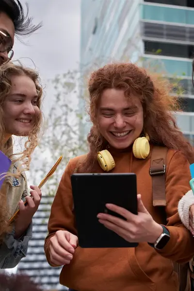 Vier studenten lachen om iets wat op een tablet zichtbaar is.